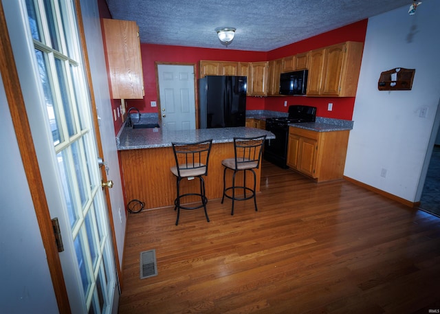 kitchen featuring kitchen peninsula, dark hardwood / wood-style floors, black appliances, a kitchen bar, and sink