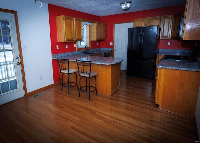 kitchen featuring sink, a breakfast bar area, a kitchen island, dark hardwood / wood-style flooring, and black appliances