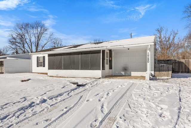 snow covered back of property featuring a sunroom and a garage