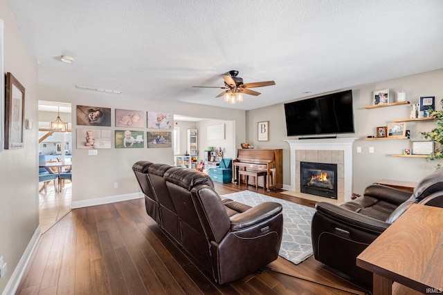 living room featuring a textured ceiling, a tile fireplace, ceiling fan with notable chandelier, and wood-type flooring