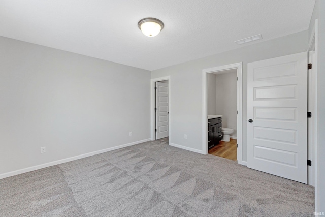 unfurnished bedroom featuring ensuite bathroom and light colored carpet