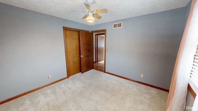 unfurnished bedroom with light colored carpet, ceiling fan, a textured ceiling, and a closet