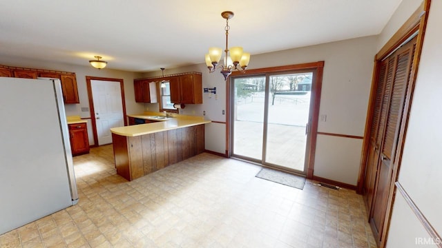 kitchen with sink, decorative light fixtures, kitchen peninsula, stainless steel fridge, and a notable chandelier