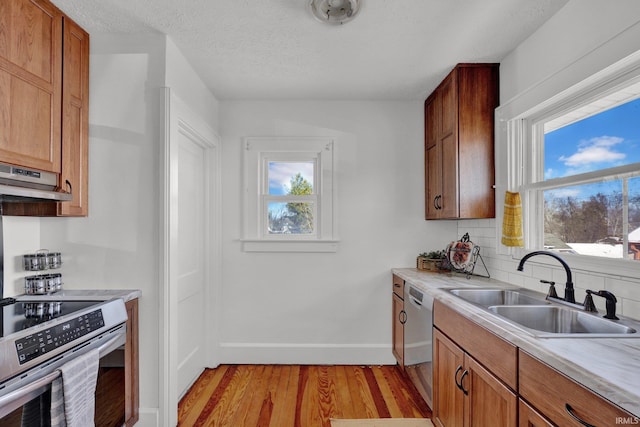 kitchen featuring a textured ceiling, light wood-type flooring, backsplash, appliances with stainless steel finishes, and sink