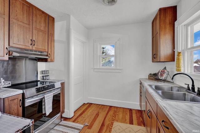 kitchen featuring stainless steel range with electric cooktop, sink, a textured ceiling, light wood-type flooring, and white dishwasher