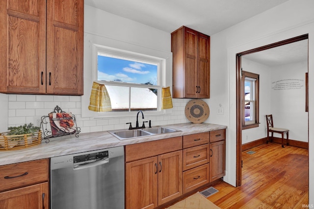 kitchen featuring sink, light wood-type flooring, stainless steel dishwasher, and backsplash