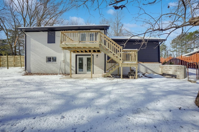 snow covered rear of property featuring french doors and a wooden deck