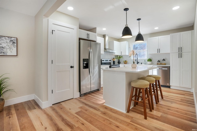 kitchen with light hardwood / wood-style floors, stainless steel appliances, a center island, white cabinetry, and wall chimney range hood