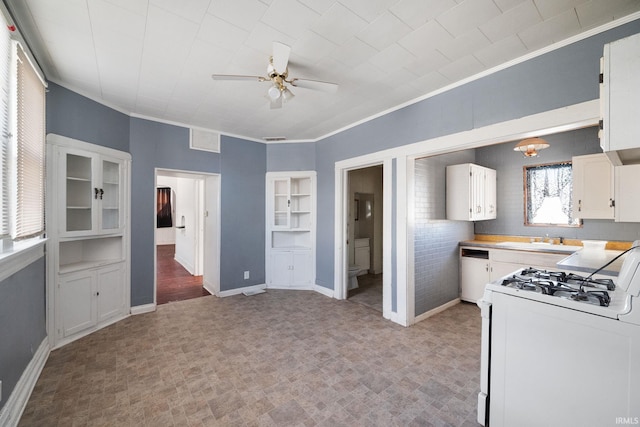 kitchen featuring crown molding, brick wall, white gas range oven, ceiling fan, and white cabinets