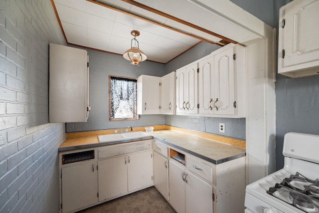 kitchen with pendant lighting, brick wall, white range with gas cooktop, white cabinets, and sink