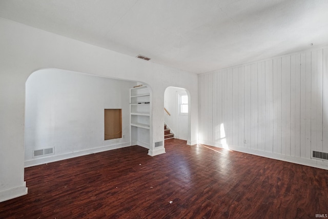 unfurnished living room with dark hardwood / wood-style flooring, wood walls, and built in shelves