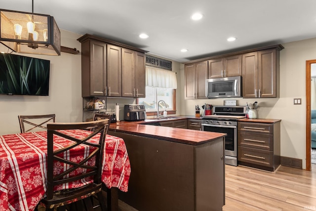 kitchen featuring stainless steel appliances, light wood-type flooring, sink, dark brown cabinets, and decorative light fixtures