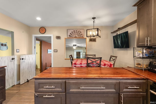 kitchen with decorative light fixtures, light hardwood / wood-style flooring, ceiling fan with notable chandelier, butcher block countertops, and dark brown cabinetry