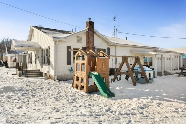 snow covered back of property featuring a playground