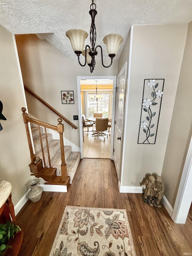 entryway with a textured ceiling, dark wood-type flooring, and an inviting chandelier