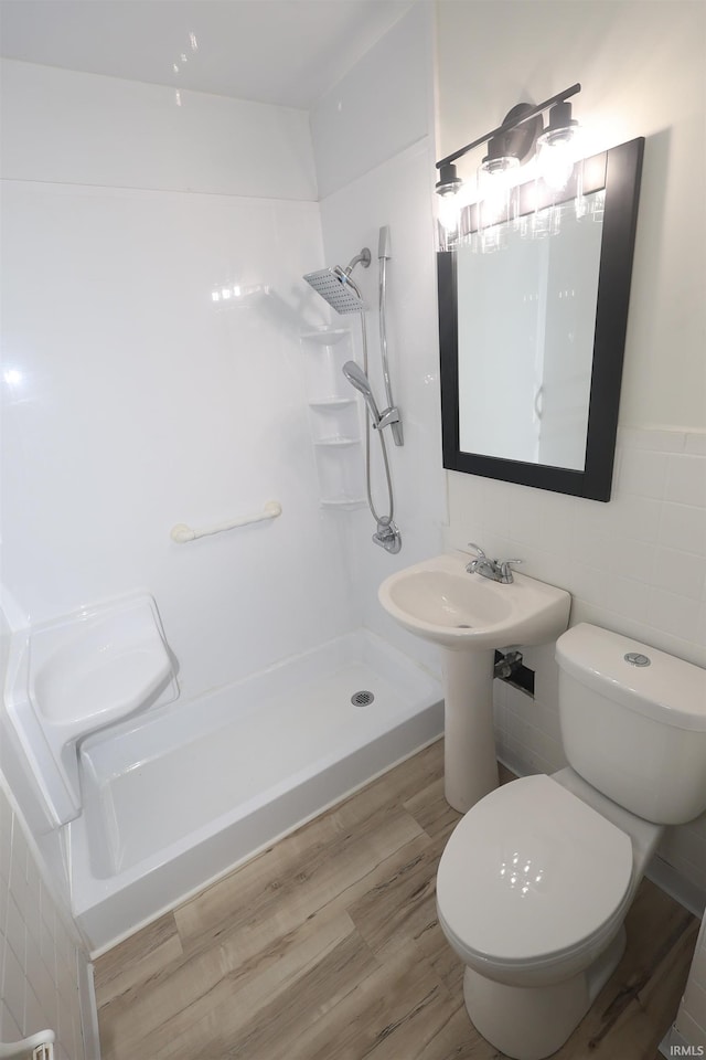 bathroom featuring toilet, hardwood / wood-style flooring, a shower, and tile walls