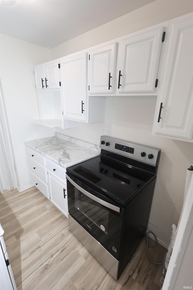 kitchen with stainless steel range with electric stovetop, white cabinets, light stone counters, and light hardwood / wood-style flooring