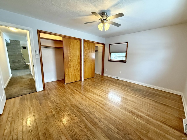 unfurnished bedroom featuring light wood-type flooring, ceiling fan, a textured ceiling, and multiple closets