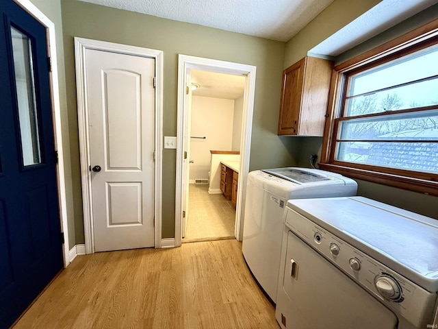 washroom with washer and clothes dryer, a textured ceiling, cabinets, and light hardwood / wood-style flooring