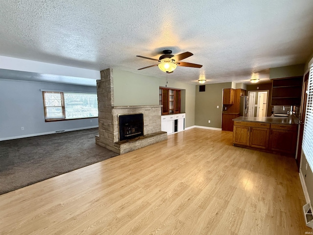 unfurnished living room featuring a textured ceiling, ceiling fan, light hardwood / wood-style flooring, and a stone fireplace