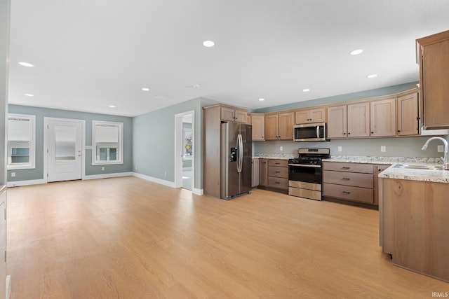 kitchen with appliances with stainless steel finishes, light wood-type flooring, light stone counters, and sink