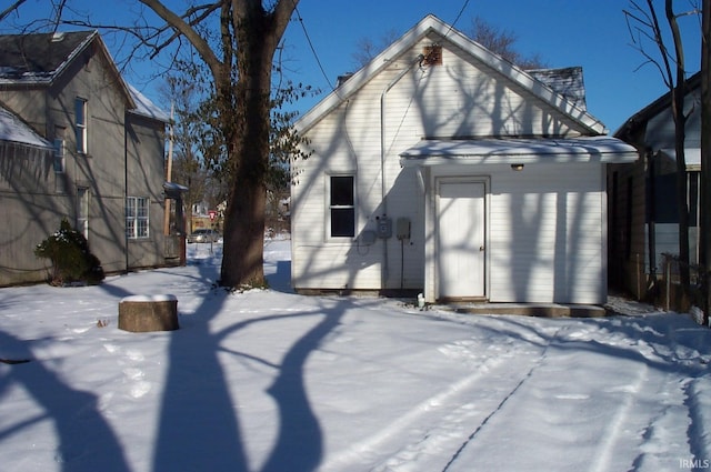 snow covered back of property featuring an outdoor structure