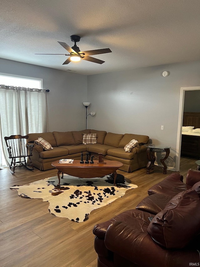 living room featuring hardwood / wood-style flooring, ceiling fan, and a textured ceiling