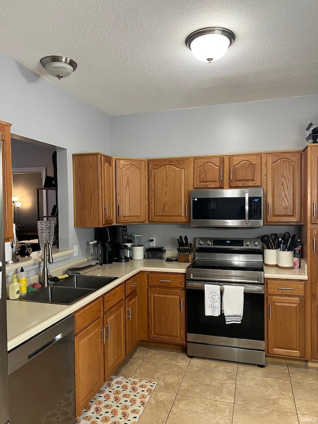 kitchen with appliances with stainless steel finishes, sink, a textured ceiling, and light tile patterned floors