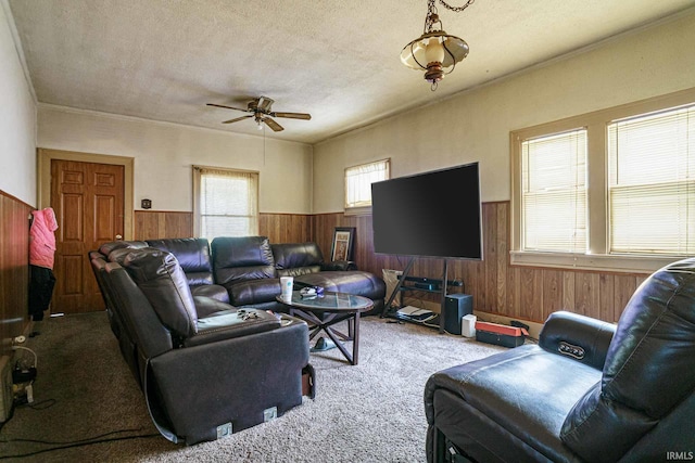 carpeted living room featuring crown molding, ceiling fan, wooden walls, and a textured ceiling