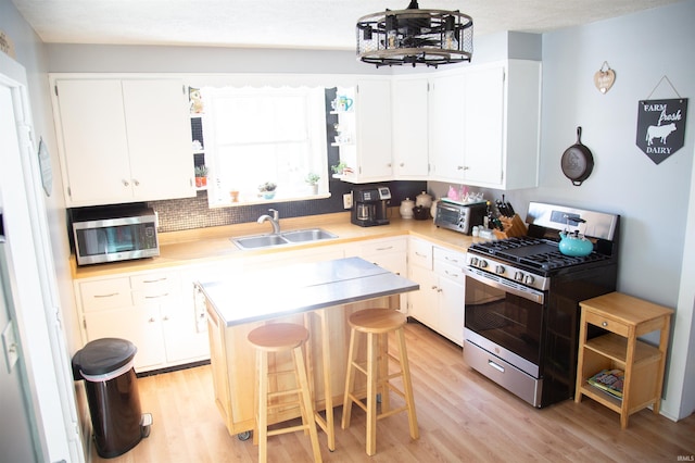 kitchen with white cabinets, appliances with stainless steel finishes, a kitchen island, sink, and a breakfast bar area