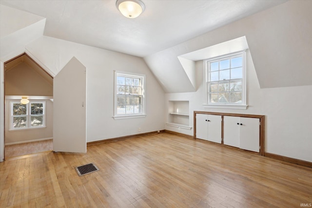 bonus room featuring light wood-type flooring, a healthy amount of sunlight, built in features, and vaulted ceiling