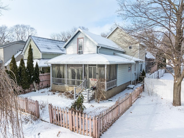 snow covered rear of property with a sunroom