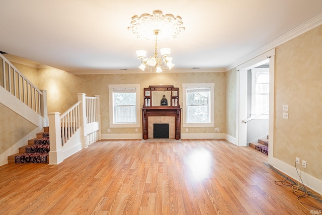 unfurnished living room featuring light hardwood / wood-style flooring, ornamental molding, a tiled fireplace, and an inviting chandelier