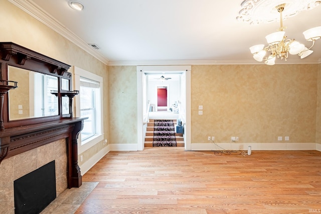 unfurnished living room featuring light wood-type flooring, crown molding, ceiling fan with notable chandelier, and a tile fireplace