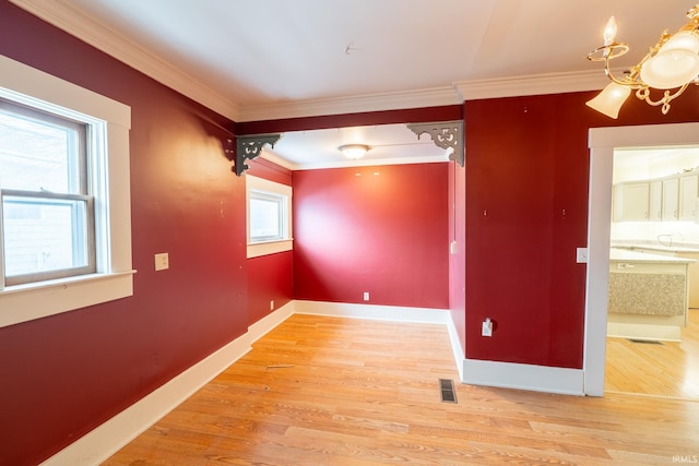 unfurnished room featuring an inviting chandelier, ornamental molding, a healthy amount of sunlight, and hardwood / wood-style floors