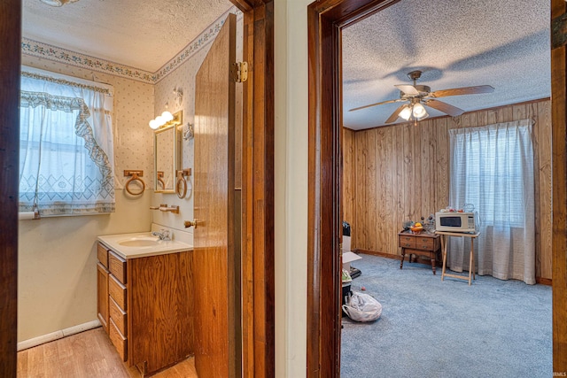 bathroom featuring ceiling fan, vanity, wooden walls, and a textured ceiling