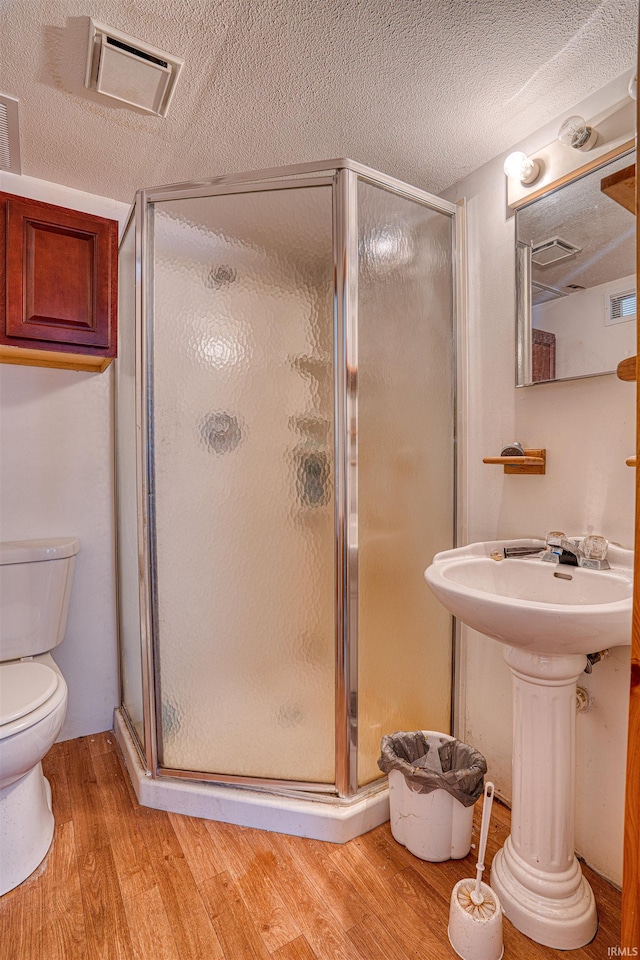 bathroom featuring wood-type flooring, a shower with shower door, toilet, and a textured ceiling