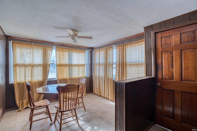 dining space with a textured ceiling, wooden walls, and ceiling fan