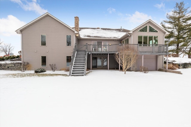 snow covered back of property with a garage and a wooden deck