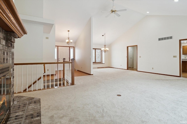 carpeted empty room with a brick fireplace, ceiling fan with notable chandelier, and high vaulted ceiling