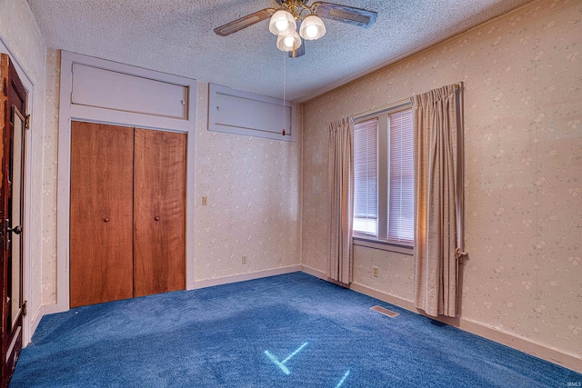 unfurnished bedroom with ceiling fan, a closet, a textured ceiling, and dark colored carpet