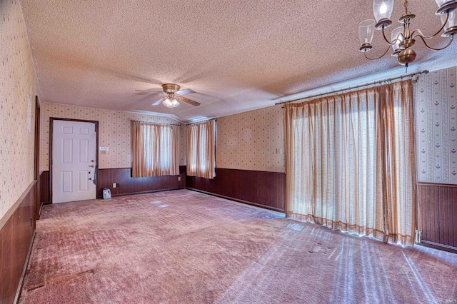 carpeted empty room with a textured ceiling, a wealth of natural light, and ceiling fan with notable chandelier