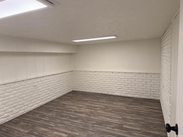 basement with dark wood-type flooring, brick wall, and a textured ceiling