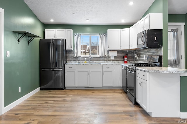 kitchen featuring a textured ceiling, appliances with stainless steel finishes, white cabinetry, light hardwood / wood-style floors, and sink