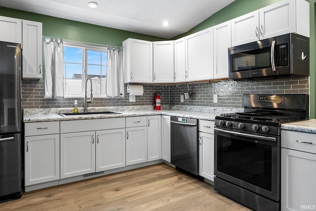 kitchen with white cabinetry, appliances with stainless steel finishes, lofted ceiling, light stone counters, and sink