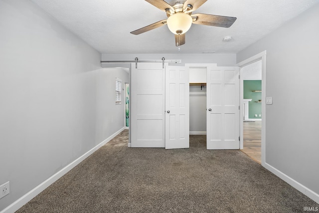 unfurnished bedroom featuring a textured ceiling, ceiling fan, a barn door, and carpet floors