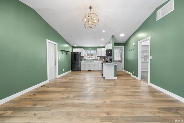 kitchen with pendant lighting, white cabinetry, light hardwood / wood-style floors, sink, and black fridge