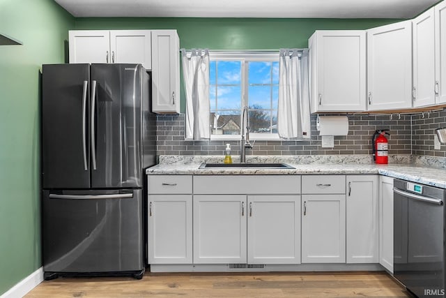 kitchen featuring light stone countertops, sink, white cabinets, and stainless steel refrigerator