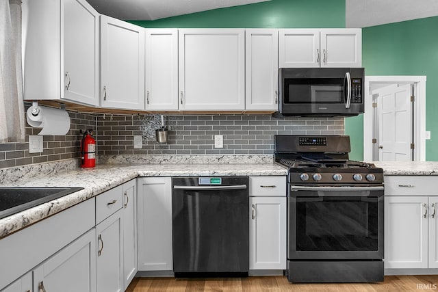 kitchen with light stone countertops, white cabinets, vaulted ceiling, and appliances with stainless steel finishes