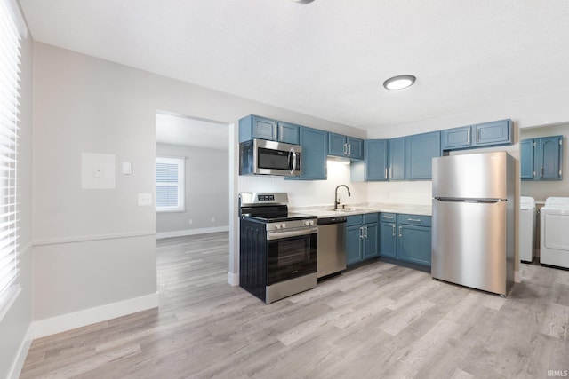 kitchen with washer and clothes dryer, appliances with stainless steel finishes, sink, and blue cabinets